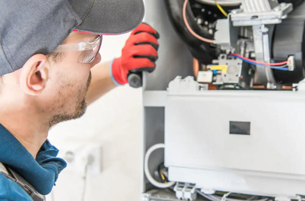 A technician wearing safety glasses, a cap, and red gloves is inspecting or repairing an open boiler or heating system, showcasing the expertise of an HVAC Contractor in Essex County, NJ, with visible wires and components inside the unit.