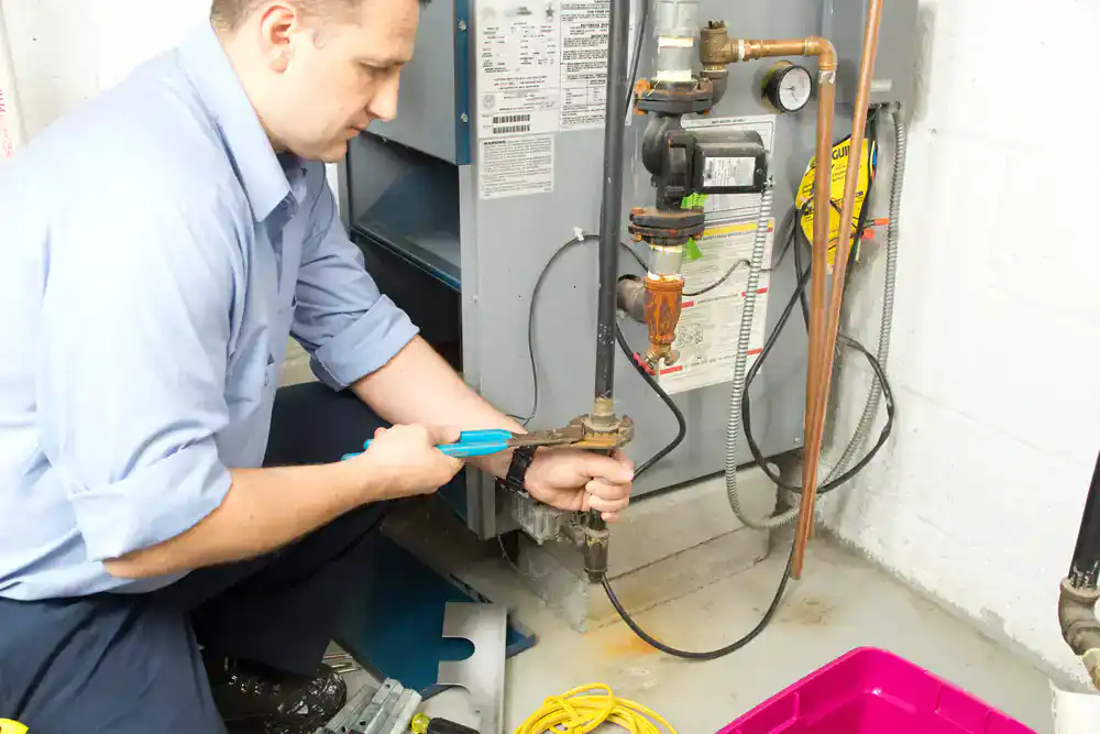 A plumber repairs piping near a water heater with a wrench, also providing HVAC services in Essex County.