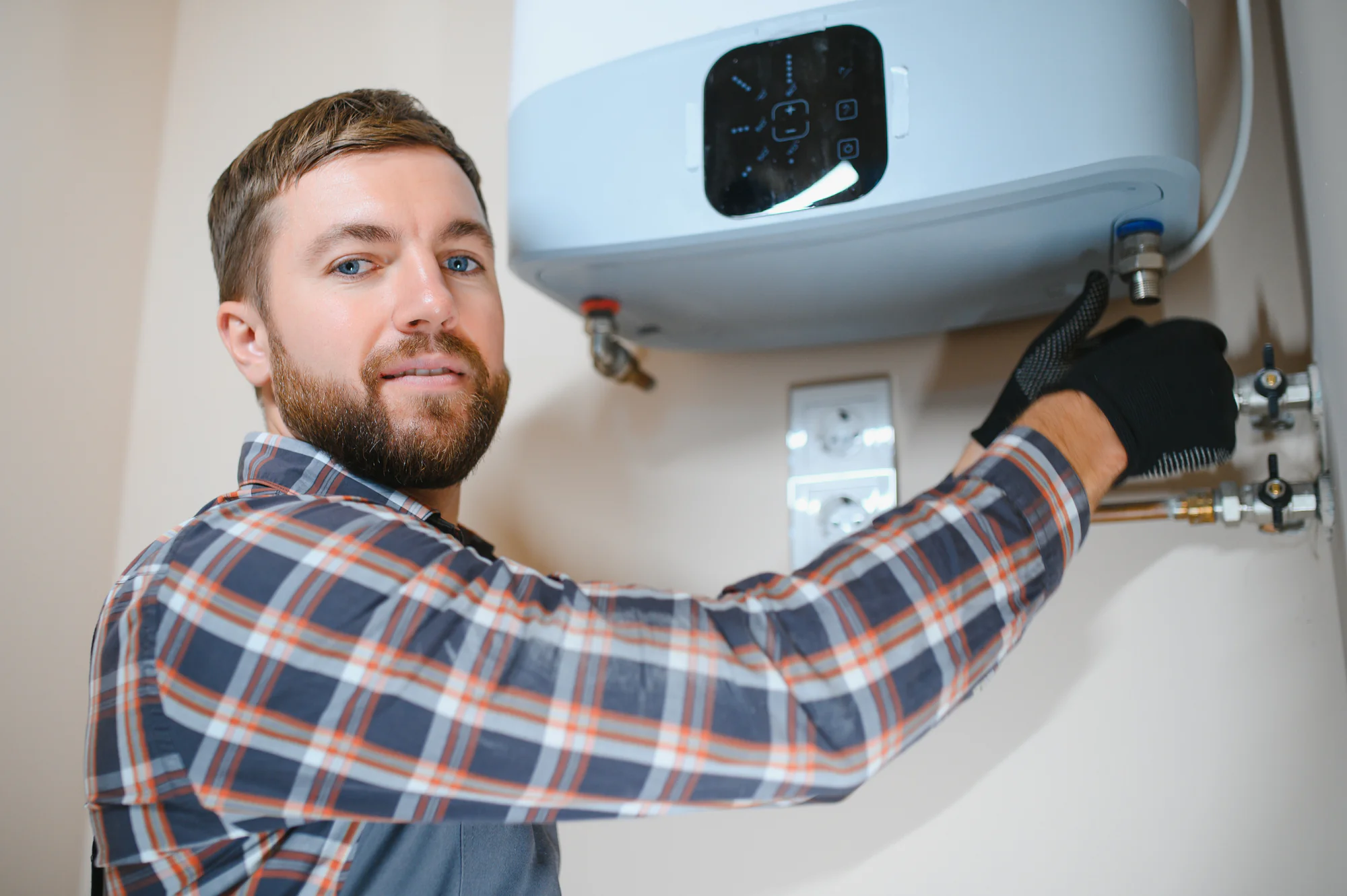 A plumber in plaid and gloves installs a water heater indoors, showcasing expert HVAC services.