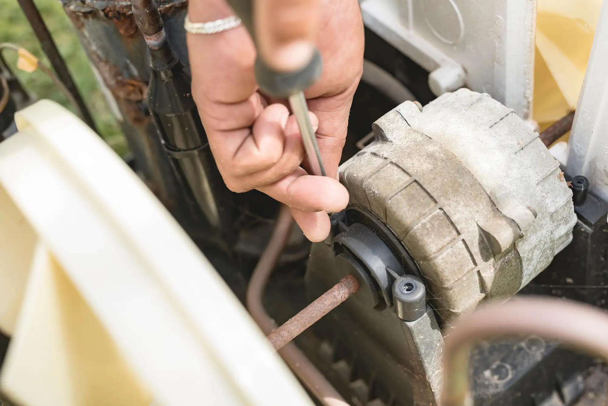 A close-up of a person's hand using a screwdriver to repair or adjust a part on a mechanical device, possibly a lawn mower or small engine.
