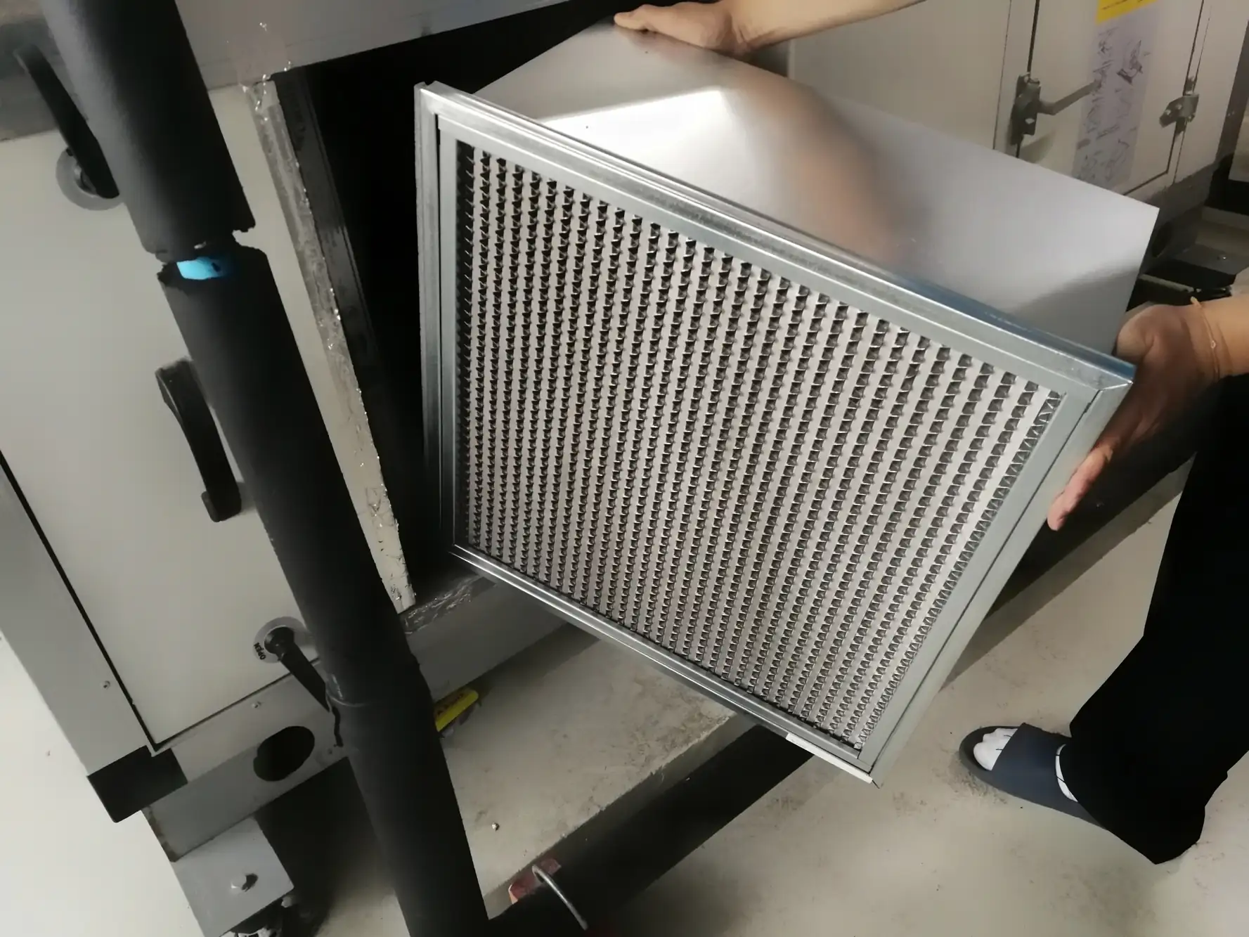 A worker installs a metal air filter into an industrial HVAC system's ventilation unit for maintenance.