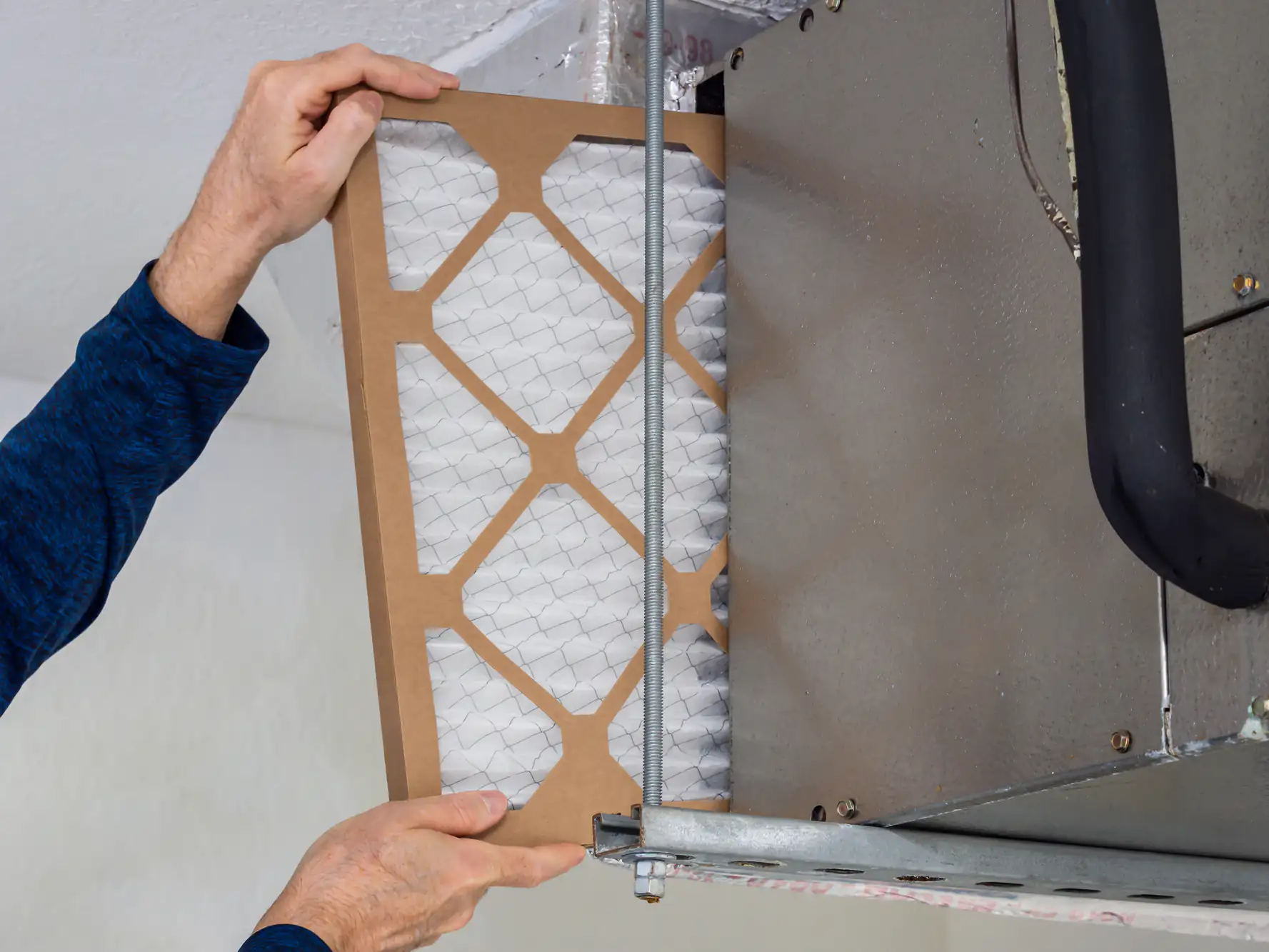 A person installs a new air filter into an HVAC system unit mounted on the ceiling for better airflow.