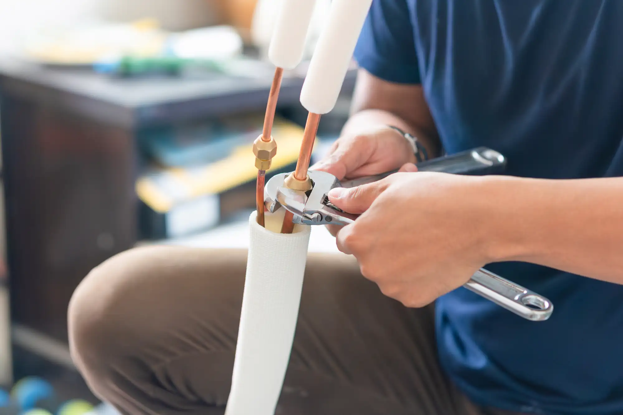 Technician uses wrenches to tighten insulated pipes, servicing an air conditioning unit.